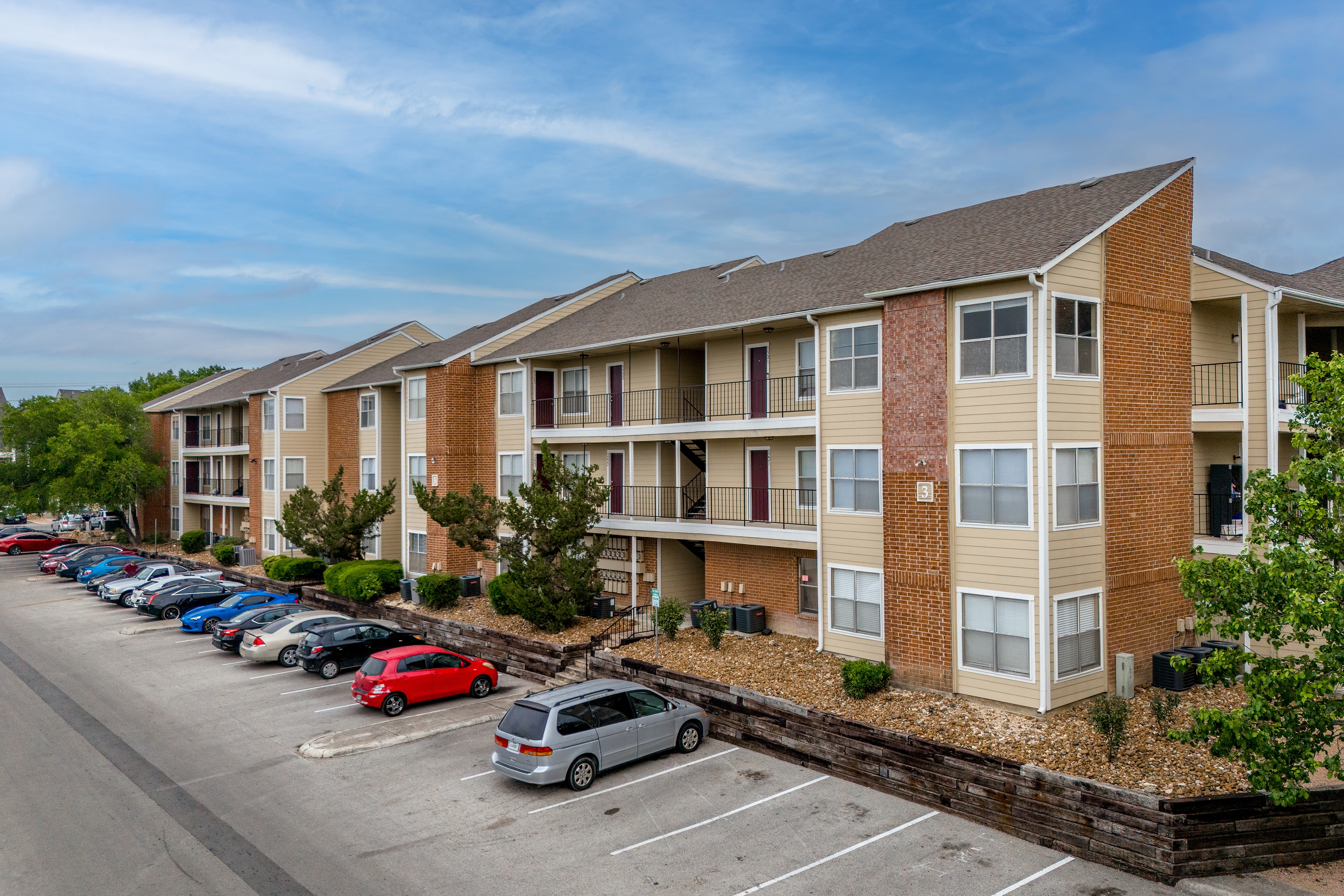 A parking lot in front of a row of apartment buildings.